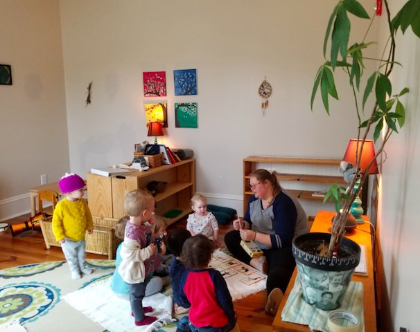 Ms. Lacey on the floor of a toddler classroom with a group of children
